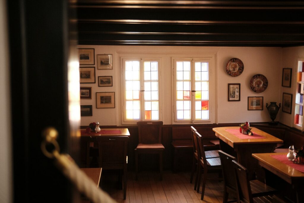Gaststube mit Holztischen, Bilderwand und Sprossenfenstern