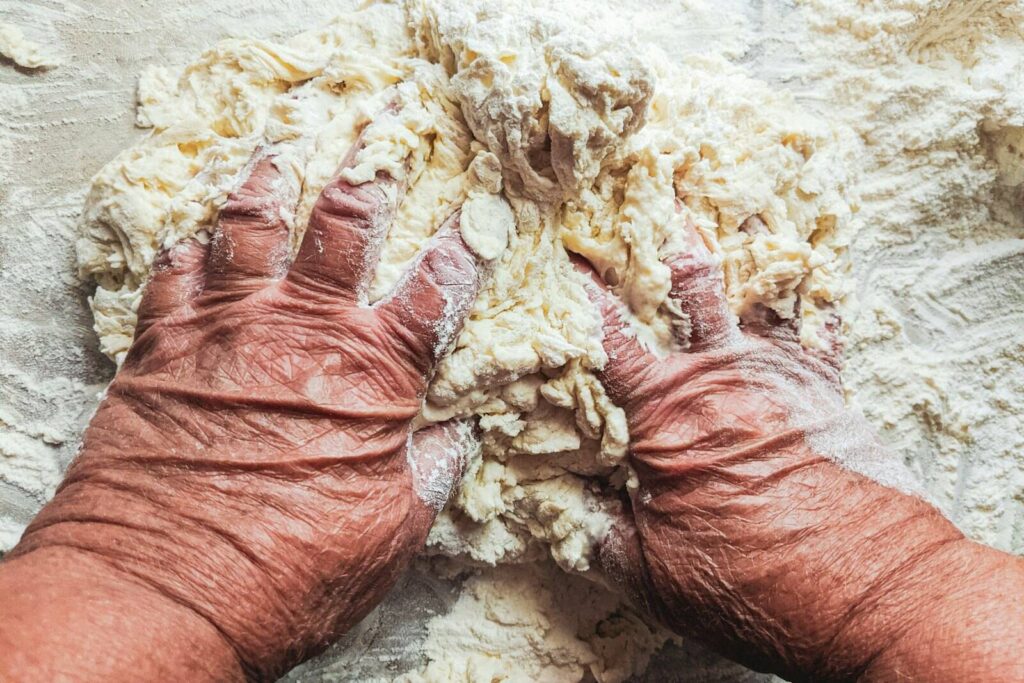 Unsere Geschichte Alte Hände kneten Teig auf einer bemehlten Arbeitsfläche
