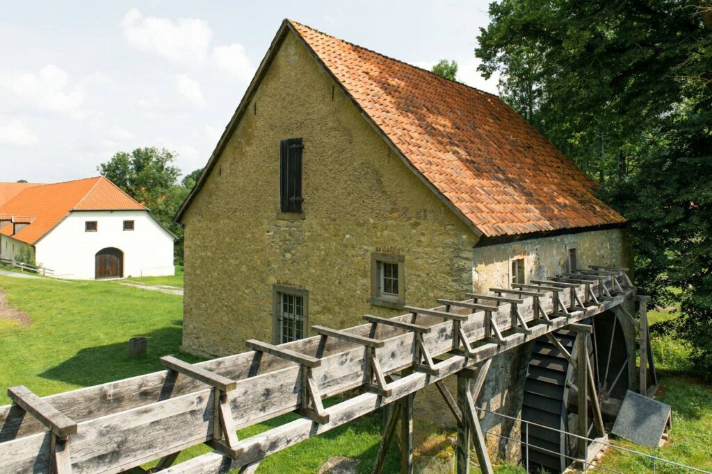 Unsere Geschichte Alte Wassermühle aus Feldstein mit Ziegeldach, hölzernem Gerinne und Wasserrad