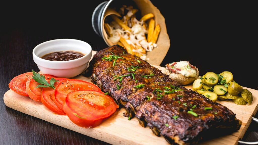 Spareribs vom Grill auf einem Holzbrett mit Tomaten und Pommes frites