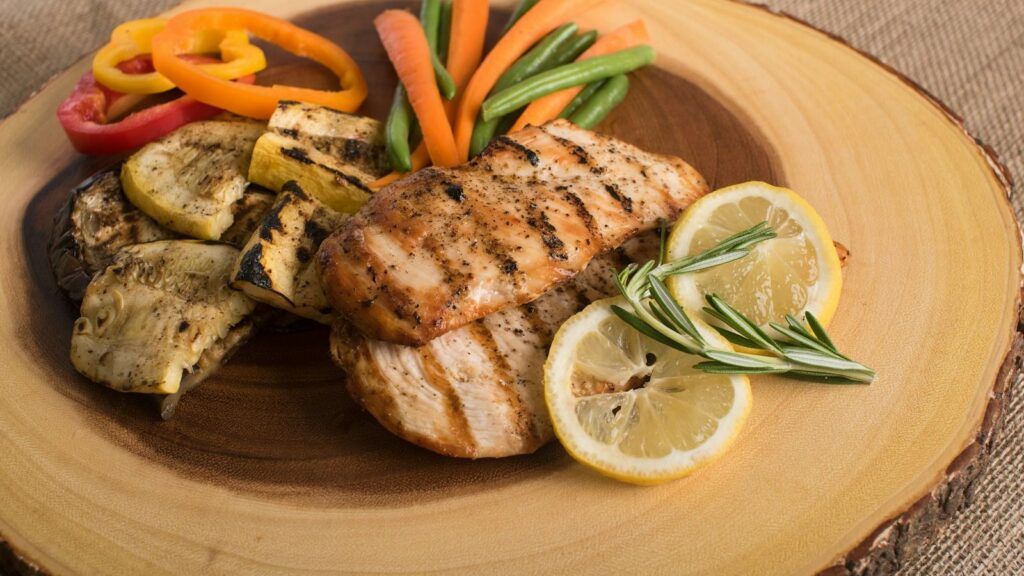 Menu Grilled chicken breast with vegetables and lemon on a wooden board