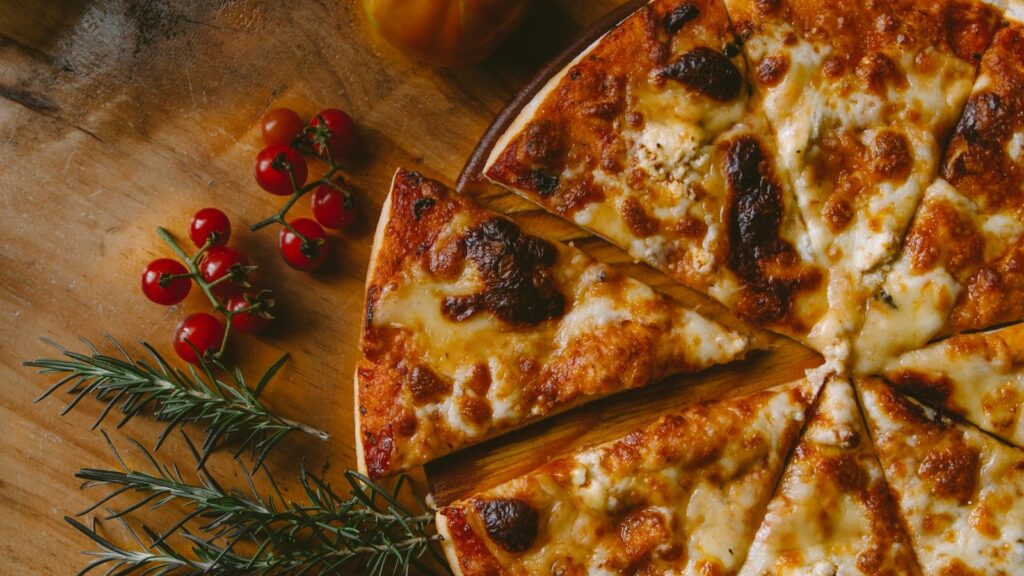 Menu Sliced pizza with cherry tomatoes and rosemary on a wooden board