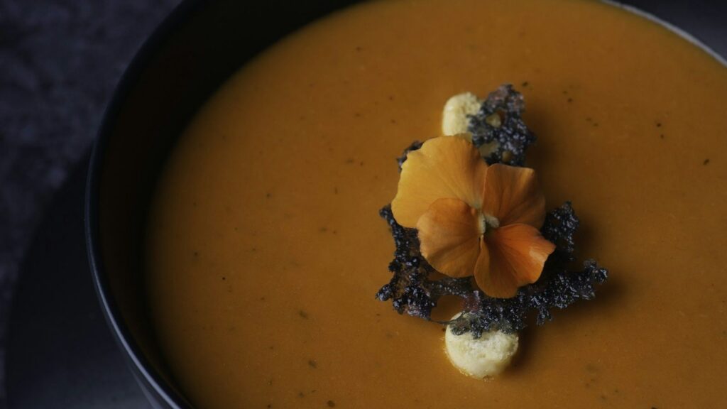 Menu Creamy pumpkin soup in a dark bowl with garnish