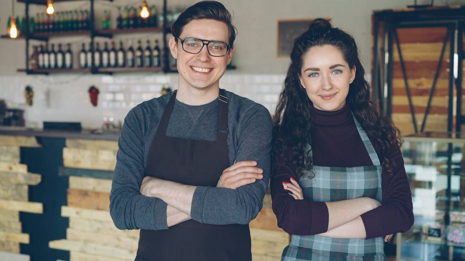 Anja Wendt und Paul Kaminski in Schürzen und mit verschränkten Armen vor dem Tresen